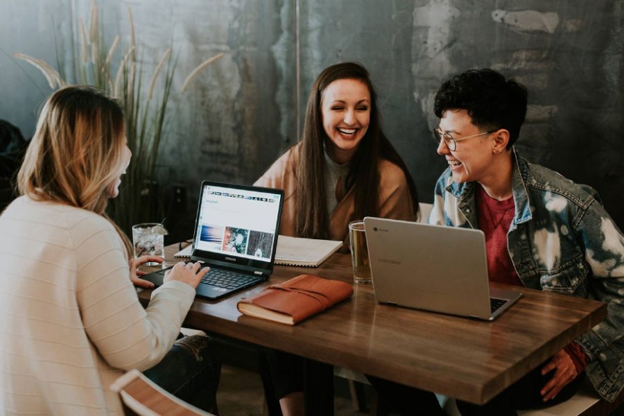 Three young adults engaging in a lively discussion at a wooden table, with laptops open, notebooks, and drinks, illustrating collaboration and social interaction related to home buying and mortgage resources.