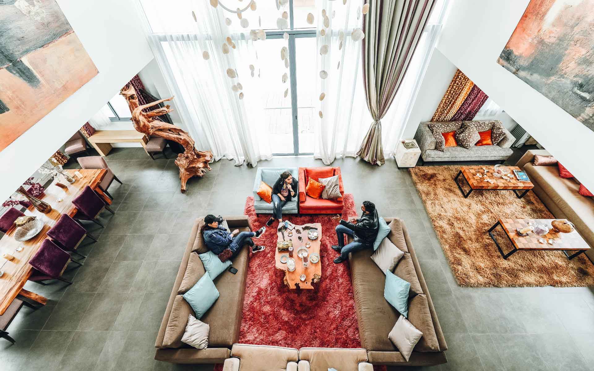 Spacious modern living room with three people conversing, stylish furniture, vibrant cushions, and large windows, showcasing the importance of quality real estate photos in attracting potential buyers.