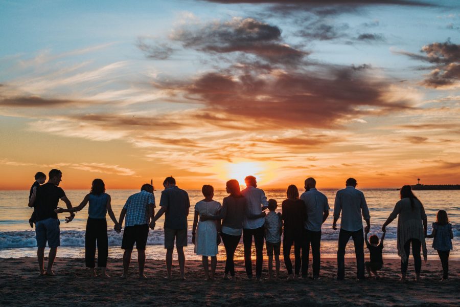 Family standing together on the beach at sunset, holding hands, with ocean waves and colorful sky in the background, symbolizing unity and togetherness.