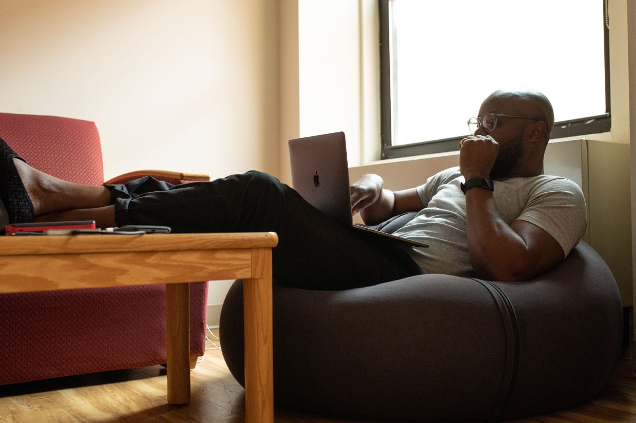 Person sitting comfortably in a bean bag chair, using a laptop to explore real estate investment options with retirement accounts like IRAs and 401Ks.