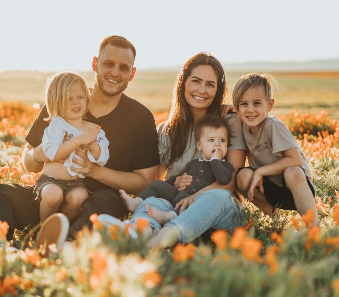 Family sitting in a field of orange flowers, smiling together, with two adults and three young children.