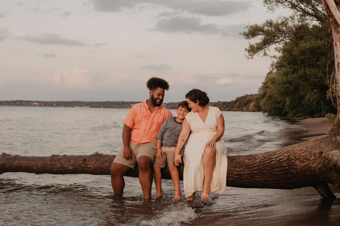 Family enjoying time together on a log by the water, smiling and connecting, with a serene lakeside background.