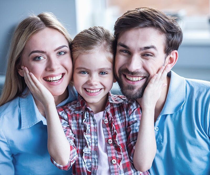 Happy family of three smiling together at home, representing the joy of family life and stability, relevant to jumbo loan benefits for purchasing high-end homes.