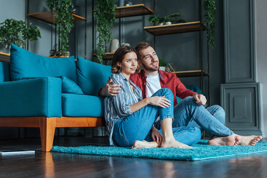 Cheerful couple sitting on a rug in a cozy living room, discussing home buying and mortgage processes.