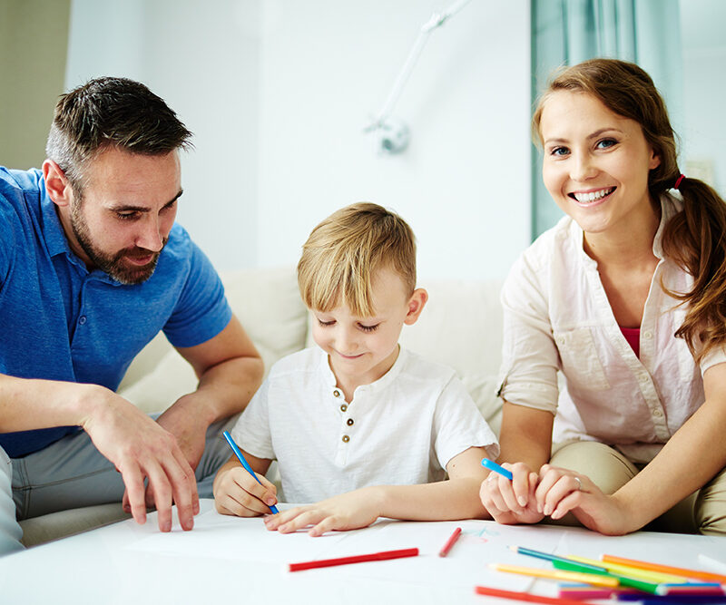 Family drawing together, child using colored pencils, parents engaging and encouraging creativity, illustrating family bonding and togetherness.