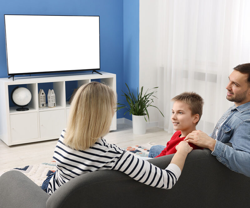 Happy family of three watching TV together in a cozy living room, emphasizing family bonding and home life, relevant to VA loan benefits for purchasing homes.